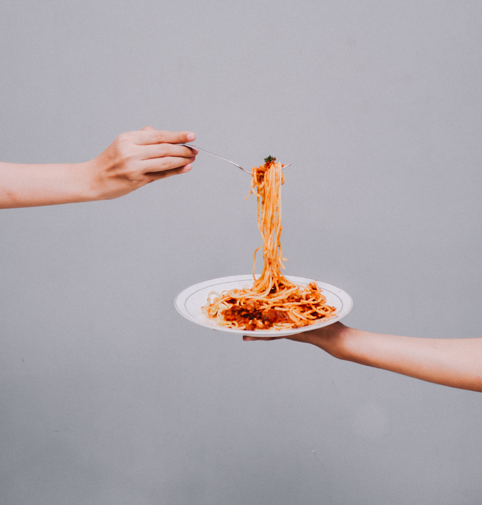 un main tenant un assiette de spaghetti et une autre avec une fourchette